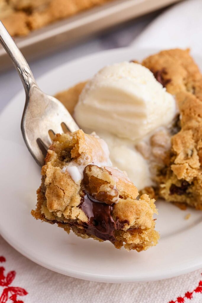 Fork holding blondie bite with vanilla ice cream in background.