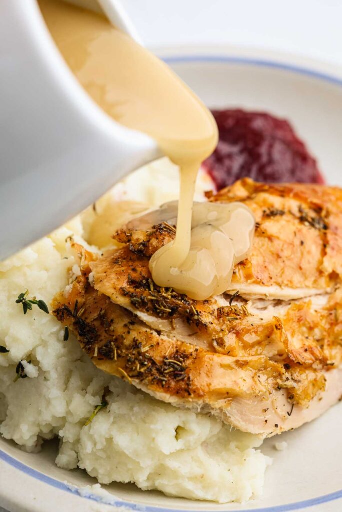 Gravy being poured on meat and mashed potatoes.
