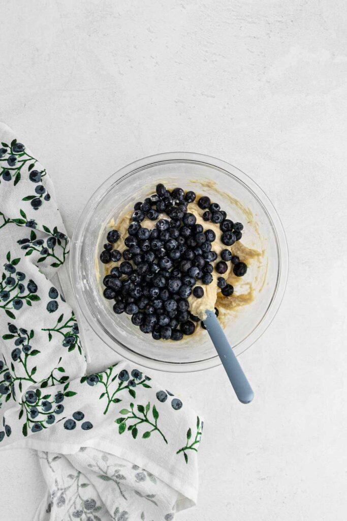 Mixing blueberries into wet ingredients, glass bowl.